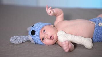 adorabile bambino dire bugie su il grande letto. bambino nel un' simpatico costume di un' cucciolo bugie e si sposta il suo poco piedi. poco ragazzo nel un' divertente a maglia costume. video