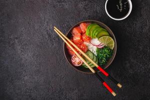 Hawaiian salmon poke salad with rice, vegetables and seaweed on black background photo