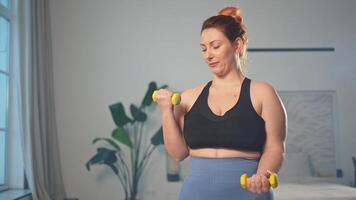 Fitness trainieren Ausbildung. Frau pflücken oben Hanteln. Plus Größe weiblich tun Sport Übung beim Zuhause drinnen. Mädchen im Sportbekleidung haben trainieren Gewicht Ausbildung zum Gewicht Verlust. Sport und Fitness video