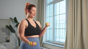 Fitness trainieren Ausbildung. Frau pflücken oben Hanteln. Plus Größe weiblich tun Sport Übung beim Zuhause drinnen. Mädchen im Sportbekleidung haben trainieren Gewicht Ausbildung zum Gewicht Verlust. Sport und Fitness video