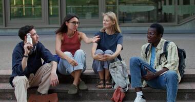 Four young people sitting on steps talking video