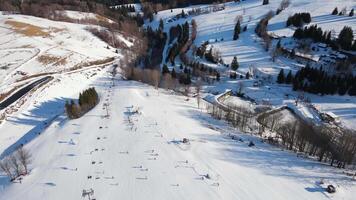 aérien vue de hiver Montagne recours avec neige couvert ski pentes, chaise ascenseurs, chalets et forêt des arbres dans ensoleillé journée. skieurs et snowboarders à ski station balnéaire. hiver des sports et Extérieur Activités video