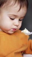 Little baby boy sitting in the feeding chair. Mom gives the spoon with porridge to her son, he takes it and stretches hand forward. Vertical video