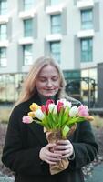 Happy International Women's Day Concept. Beautiful happy Caucasian woman smelling bunch of tulips with closed eyes video