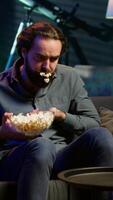 Vertikale Mann im Wohnung erstickend auf Essen während Aufpassen Film auf Fernseher und Essen Popcorn. Person bekommen Kehle verstopft während schlucken Snack, tun heimlich Manöver auf Couch, Kampf zum seine Leben, Kamera ein video