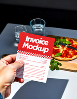 A hand holds a red invoice mockup with a partially visible pizza in the background psd