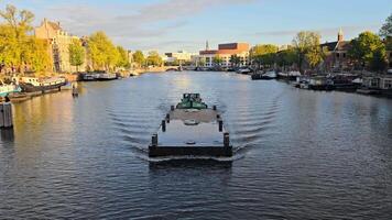 amsterdam. Olanda 11.11.2024 carico chiatta andare in barca su amsterdam fiume, circondato di storico edifici e Barche sotto d'oro tramonto leggero video