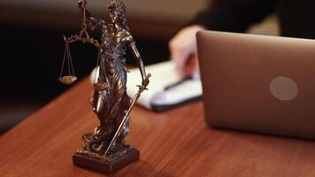 Golden lady justice statue is displayed on a wooden desk in a law office, symbolizing justice, fairness, and the legal system. Statue of Themis with a pair of scales of justice. Advertising video