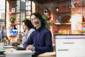 Portrait of cheerful Asian call center agent talking with customer, adhering to company communication guidelines. Jolly experienced customer support worker follows call script during chat with client photo
