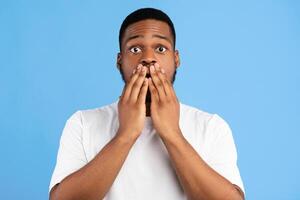 Omg. Shocked Black Guy Covering Mouth With Hands Posing Looking At Camera On Blue Background. Studio Shot photo