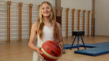 caucasien écolière enfant lancement Balle Jeune enfant fille élève jouer sport physique éducation sportive fille content prendre plaisir basketball Jeu étudiant souriant en jouant Université école classe adolescent Gym video