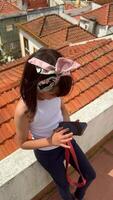 A young child sitting on a rooftop with a phone in one hand and a bow in the other, video