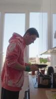 une Jeune homme joyeusement cuisine dans une moderne et élégant cuisine rempli avec Naturel lumière video