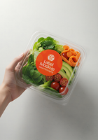 A hand holds a clear container of fresh salad with a label that says Label Mockup Salad Packaging psd
