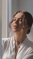 bruid glimlachen door zonovergoten venster in wit gewaad, een bruid in een wit gewaad glimlacht net zo ze staat door een zonovergoten venster video