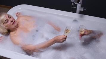 Sénior couple grand-père et grand-mère est prise mousseux une baignoire en buvant Champagne dans luxe salle de bains video