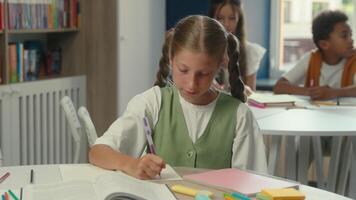 souriant content caucasien fille adolescent fille école enfant enfant élève écolière à classe table l'écriture tâche examen devoirs primaire éducation leçon les enfants en train d'étudier apprentissage positif à la recherche à caméra video