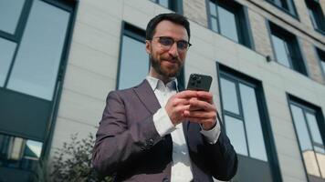 souriant caucasien homme d'affaire content satisfait Masculin employeur homme en utilisant mobile téléphone envoyer des SMS messages affaires bavarder commerce électronique travail avec téléphone intelligent en plein air près Bureau entreprise réservation Taxi dans ville video